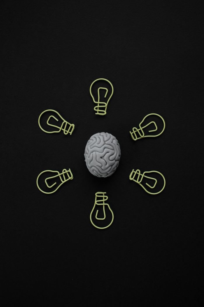 approach-img Top view of a brain model surrounded by paper clip light bulbs on black background.